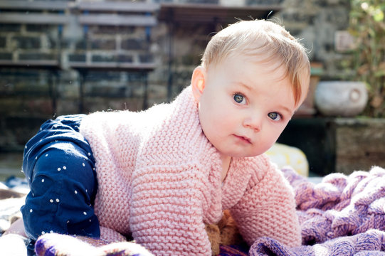 Portrait of baby girl crawling on knitted blanket in garden