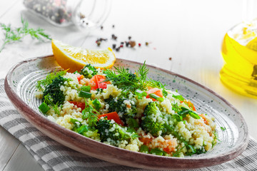 Healthy salad made of couscous, broccoli, tomato, pepper, onion and dill on a table. Traditional Moroccan food for healthy meal. Close-up shot.