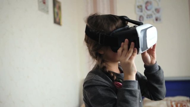 A cute little girl uses a virtual reality VR helmet with pleasure. Girl mastering the new technology