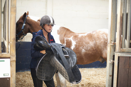 Young woman removing saddle from horse
