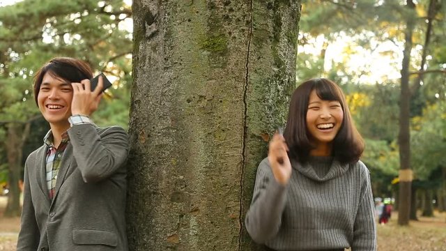 幸せカップルイメージ　木陰でスマホで告白して向き合う　笑う　公園