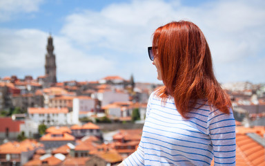 Red haired girl is photographed on a background of colorful red roofs houses in Europe in Porto, Portugal