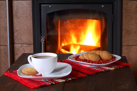A mug of tea and plate of biscuits are on the table in front of the fireplace.