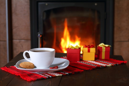 A mug of tea and gift boxes are on the table in front of the fireplace.