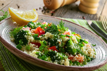 Vegetarian salad made of couscous, broccoli, tomato, pepper, onion and dill on a plate. Traditional Moroccan food for healthy meal on a table. Close-up shot.
