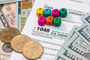 tax form with wooden cubes, dollar bills, coin.