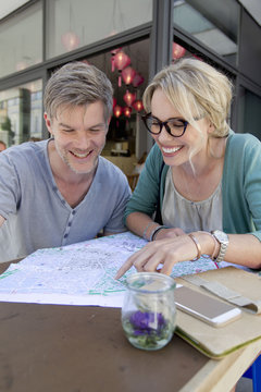 Couple pointing at map on city sidewalk cafe table