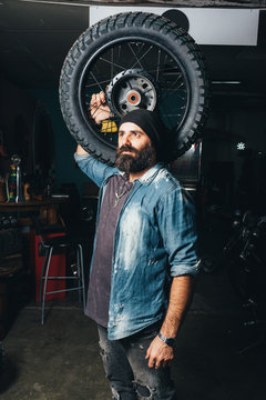 Portrait of mature man, in garage, holding motorcycle tire