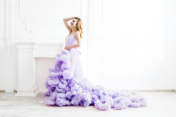 Dreamy woman portrait in a long pale purple ruffled gown in a white room. Elegant femininity