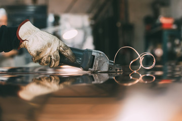 Hands of metalworker gouging sheet copper at forge workbench