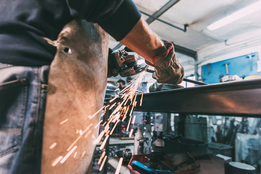 Mid section of metalworker grinding metal rod in forge workshop