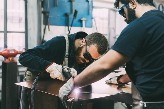 Metalwork team cutting copper with welding torch in forge workshop