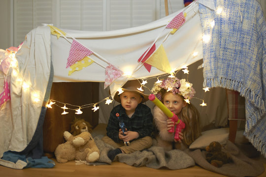 Girl and brother hiding in den with toy guns