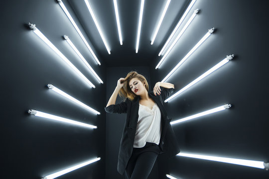 Young fashion model posing in studio, electric lighting behind her