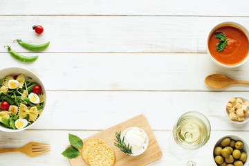 Light summer dinner / supper concept. Green salad with pasta, cherry tomato, quail eggs. Cold tomato soup (gazpacho), croutons, green olives, crackers and glass of cold white wine. 