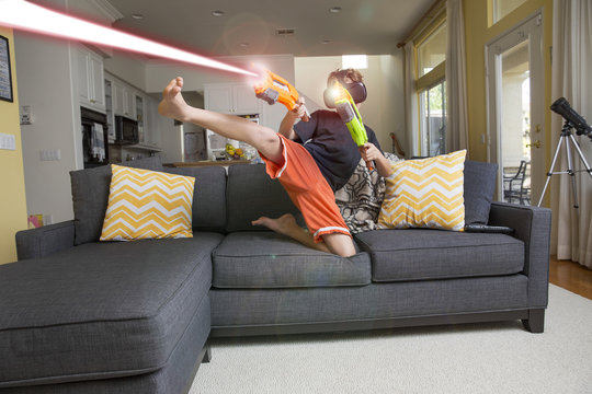Young boy on sofa, wearing virtual reality headset, kicking leg, firing laser guns, digital composite