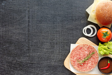 Raw minced beef (patty) with herbs, sesame bun, cheese, tomato, lettuce, onion, hot BBQ sauce, chili. Homemade hamburger ingredients. Black background. Space for text.