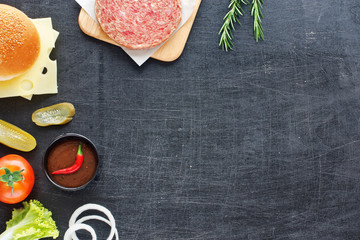 Handmade minced beef burger, bun, cheese, tomato, lettuce, onion, pickle, hot BBQ sauce. Black board background. Space for text.