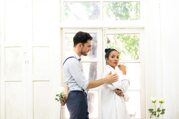 Young man trying to reconcile his girlfriend offering white rose in the white room..
