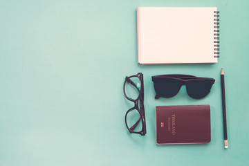 Flat lay design of work desk with notebook, glasses and passport on green background.