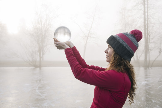 Woman holding up crystal ball on frozen lake
