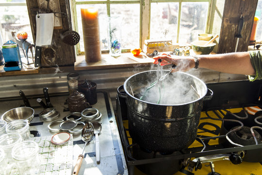 Woman using tongs to remove preserves jar from steaming saucepan