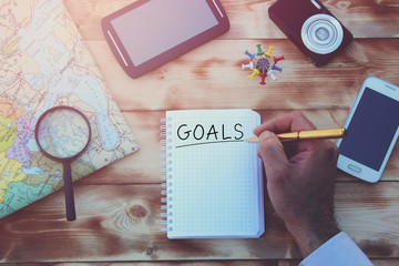 Hand writing goals for travel, compass and map on a wooden table