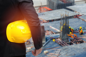 double exposure of businessman hold in hand yellow safety helmet  industrial concept on blurred construction site workers background, color tone effect.