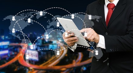 smart businessman in suit using his tablet, business and technology concept with world map social media network connection on blurred night city background, color tone effect.
