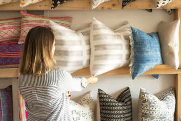 Rear view of female interior designer adjusting cushions on shelves in retail studio