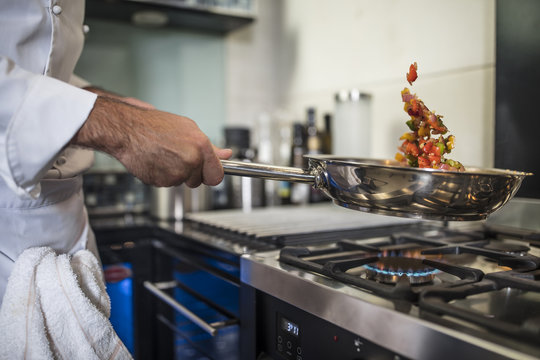 Chef holding frying pan, cooking food over stove, close-up