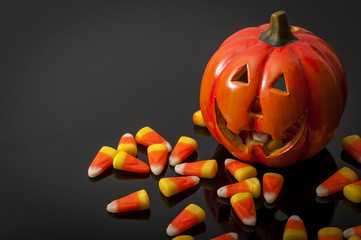 Halloween and Trick-or-treating concept with Jack-o-lantern surrounded by candy corn on black background with copy space