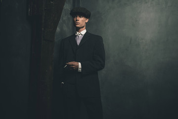 Retro 1920s english gangster standing with cigarette. Wearing suit and flat cap.