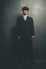 Retro 1920s english gangster standing with cigarette. Wearing suit and flat cap.