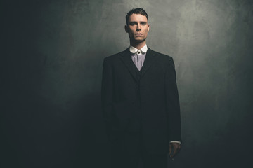 Retro 1920s english gangster in suit standing with cigarette.