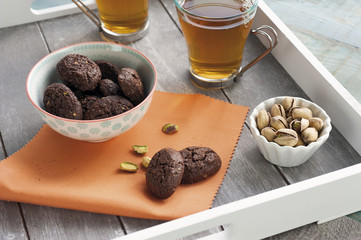 rustic biscuits with chocolate and nuts in ceramic cup, served on wooden tray with two cups of tea and a cup of fresh pistachio nuts