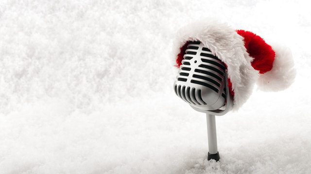 Carols and Christmas music concept with a microphone wearing a santa hat isolated on white snow with copy space