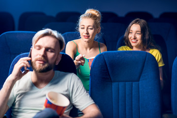 Rude man talking with phone disturbing women on the back seats in the cinema