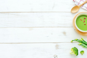 Green vegetable soup, broccoli, onion, wooden spoon on a white table. Top view. Place for text.