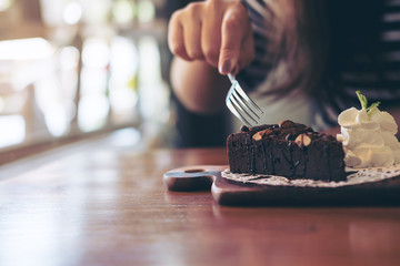 A woman's hand cutting brownie cake with fork in vintage wooden cafe