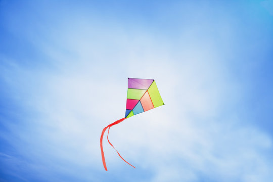 angle view of a colorful kite flying with waving red bow in a deep blue sky with the light of the sun