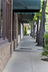 Obraz premium View of empty cement sidewalk leading through trees and various shops.