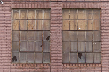 Twin windows showing signs of abandonment on a vintage red brick building.