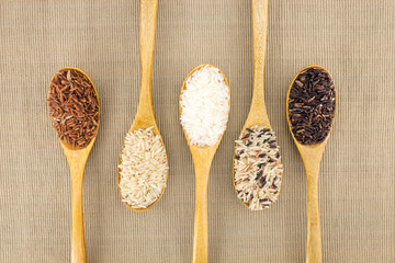 Jasmine rice, Brown rice, Red rice, Mixed rice and Riceberry in wooden spoons.