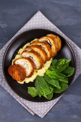 Chicken Kiev on mashed potato with spinach. Breaded chicken breast stuffed with herbs and butter on black plate. View from above, top studio shot