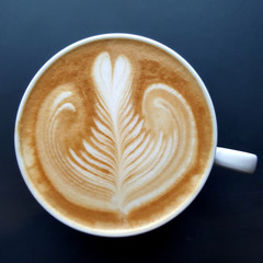 Top view of a mug of latte art coffee on black background.