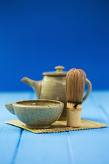 Ceramics bowl and chasen - special bamboo matcha tea whisk, lying on blue wooden background.