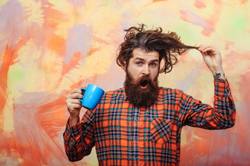 surprised bearded man pulling stylish fringe hair with blue cup