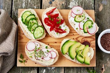 Healthy sandwiches with avocado, cherry tomato, cucumber, radish,cream cheese and flax seeds. On a wooden cutting board, top view. Healthy vegetarian snack