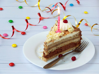 piece of chocolate banana cake decorated with rosettes of cream, berries and candles on light wooden background. Birthday.